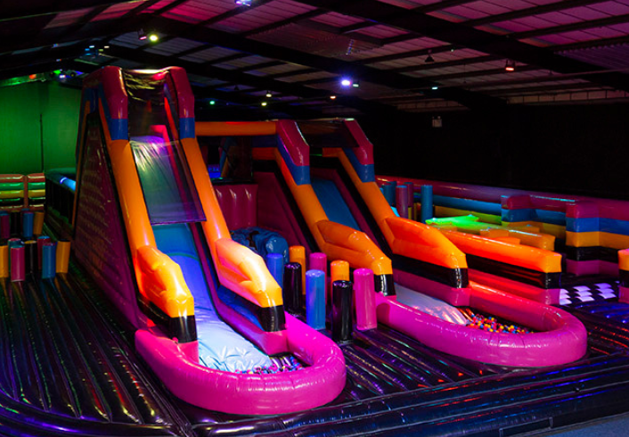 Double inflatable slides with colourful neon design in an indoor inflatable park – ideal for climbing and sliding