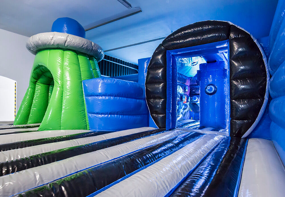 Inflatable obstacle with green UFO structure and black-blue tunnel in an indoor inflatable park