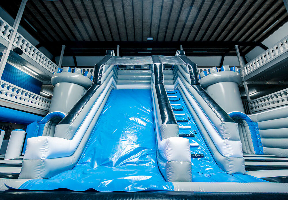 Large inflatable slide in castle theme with blue and grey colours in an indoor inflatable park
