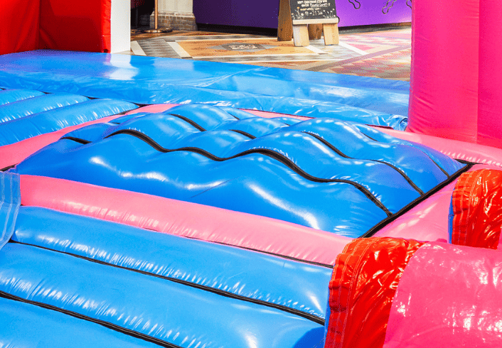 Wave runner obstakel in inflatable park – blauw en roze opblaasbare baan met golvend oppervlak voor rennen en springen